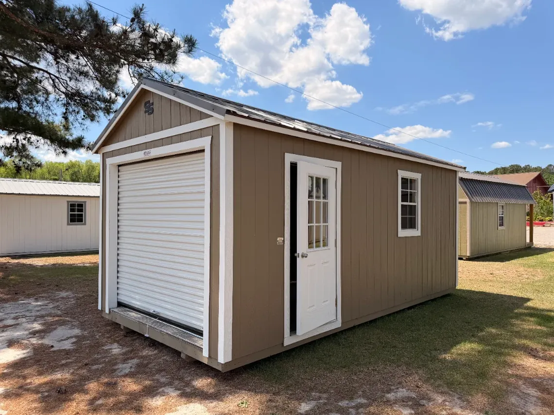 Tan workshop shed with a white roll-up garage door beside a single entry door
