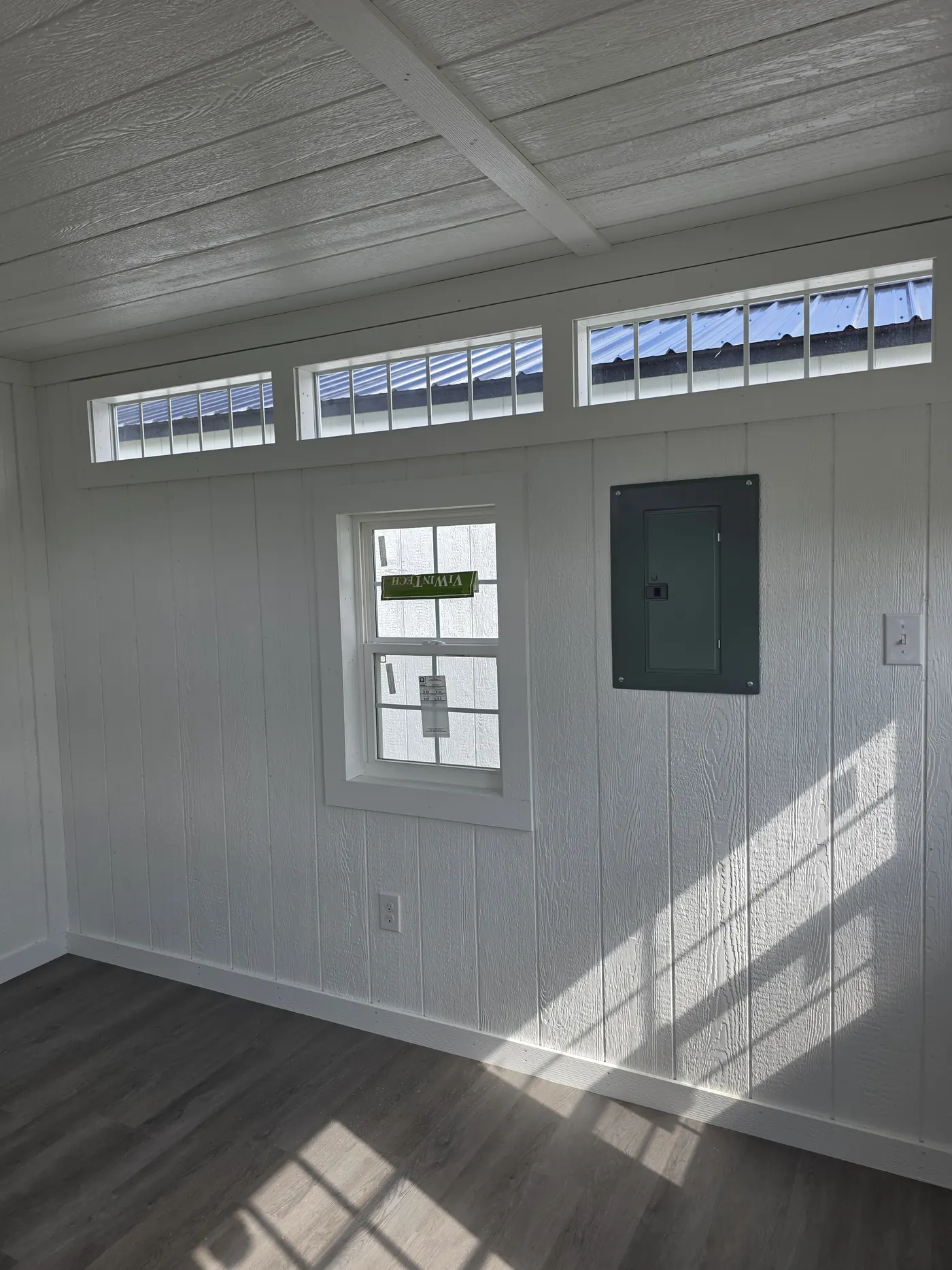Inside a finished shed showing the breaker panel, wall outlets and transom windows from an electrical package